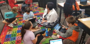 Students working on their laptops around the teacher